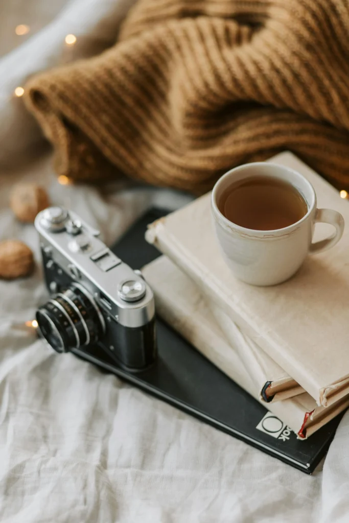 A stack of books and notebooks with a cup of tea on top with a vintage camera off to the side.